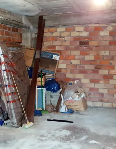 Vista del garaje antes de la reforma, con paredes de ladrillo y desorden de materiales.
