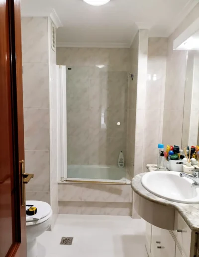 Imagen de un baño antiguo, con azulejos blancos y grises, una bañera con mampara de vidrio y un lavabo en encimera de mármol.