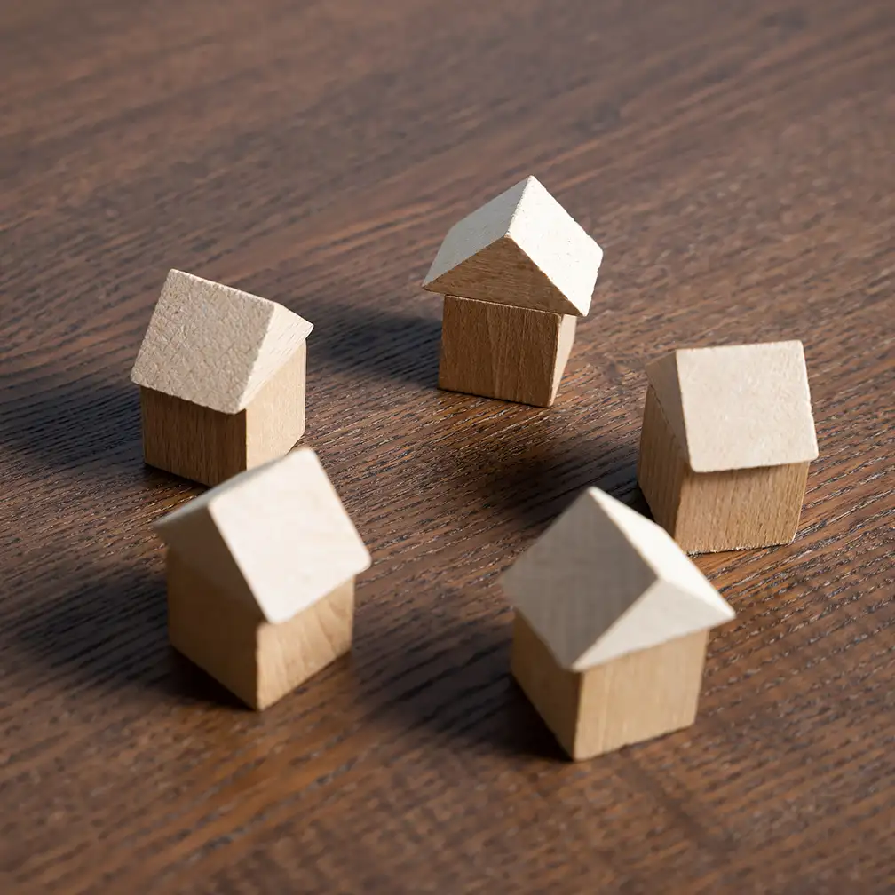 Cinco pequeñas casas de madera en círculo sobre una mesa de madera, representando la gestión de propiedades.