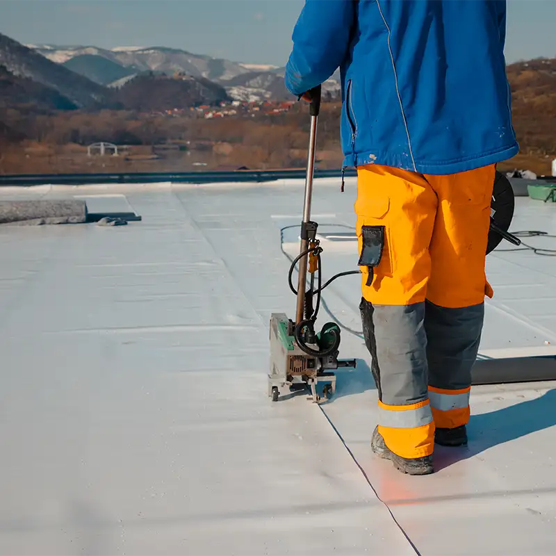 Trabajador realizando la impermeabilización de una cubierta plana con equipo especializado, en un entorno montañoso.