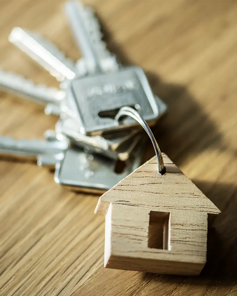 Llaves de una vivienda con un llavero en forma de casa, sobre una mesa de madera.
