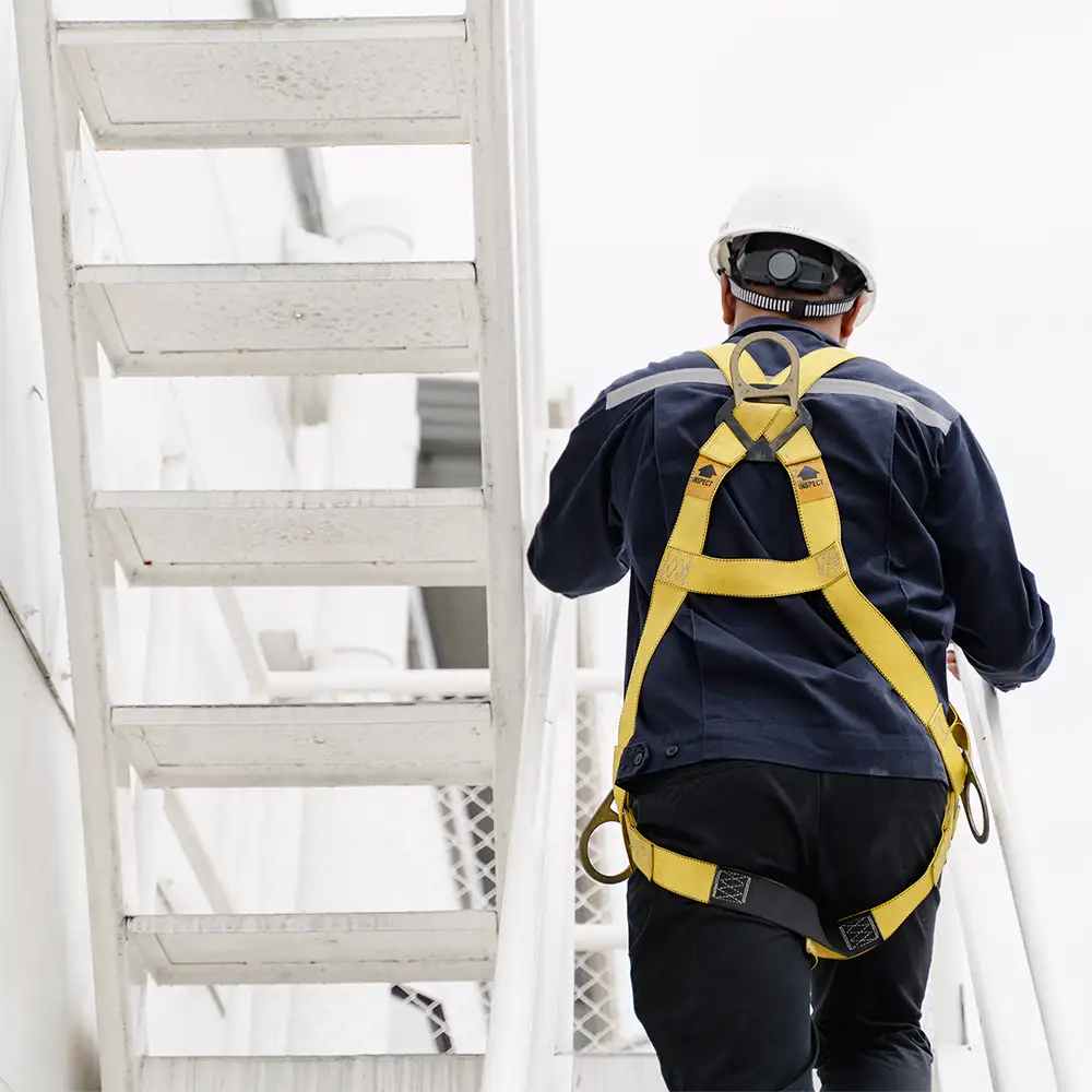 Trabajador de mantenimiento subiendo una escalera con equipo de protección y arnés de seguridad